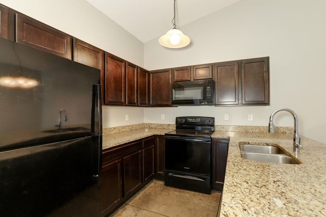 Kitchen with vaulted ceiling, decorative light fixtures, sink, black appliances, and light stone countertops | Image 8