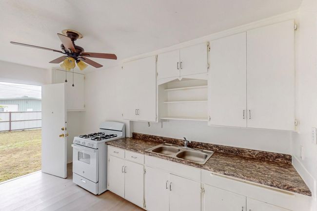 Kitchen with open shelves, white gas range oven, dark countertops, ceiling fan, and light wood-style flooring | Image 9