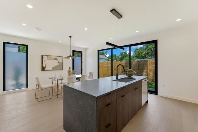 Kitchen with modern cabinets, light wood-style floors, a large island with sink, recessed lighting, and dark countertops | Image 12