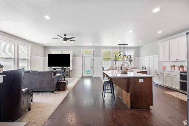 Kitchen featuring ceiling fan, a wainscoted wall, white cabinets, light countertops, and a kitchen island with sink | Image 5
