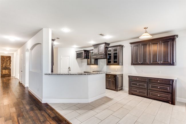 Kitchen featuring backsplash, dark brown cabinets, light hardwood / wood-style floors, light stone counters, and custom range hood | Image 9
