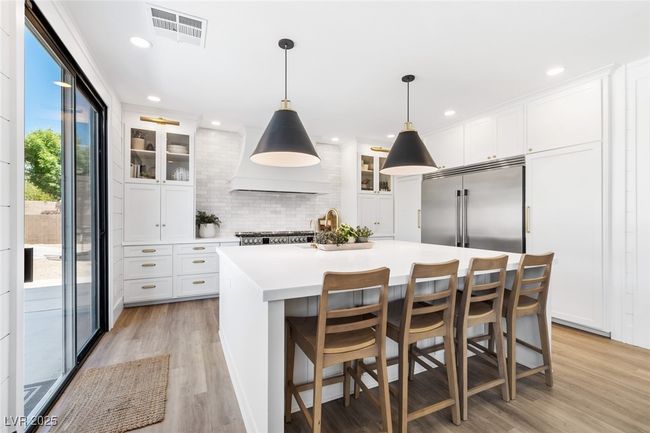 Kitchen featuring built in refrigerator, tasteful backsplash, light wood-style floors, wall chimney exhaust hood, and visible vents | Image 12