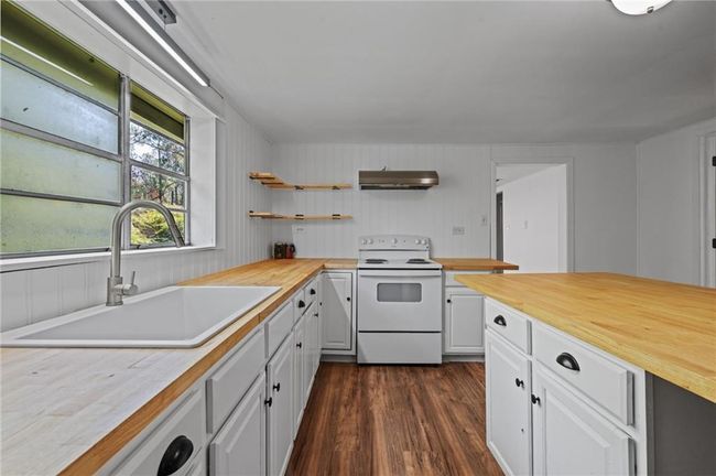 Kitchen featuring white electric range, wood counters, under cabinet range hood, white cabinets, and dark wood-style flooring | Image 10