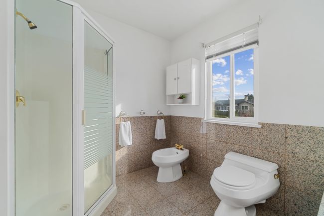 Bathroom featuring a wainscoted wall, tile walls, toilet, a stall shower, and a bidet | Image 25