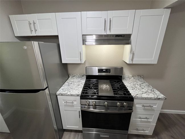 Kitchen with appliances with stainless steel finishes, under cabinet range hood, white cabinetry, and dark wood-style flooring | Image 8