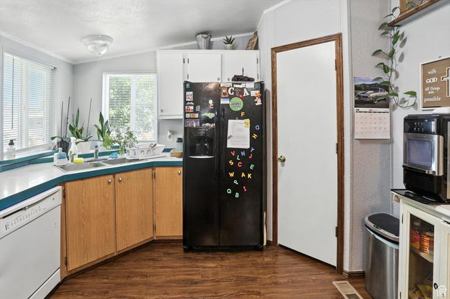 Kitchen featuring black fridge with ice dispenser, dishwasher, dark wood-type flooring, ornamental molding, and light countertops | Image 8