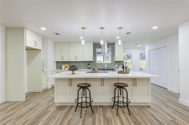 The breakfast bar on one side of the island is perfect for casual meals, offering seating for family and guests while allowing for easy conversation with the cook. The Quartz countertops extend across the island, complemented by the sleek green subway tile backsplash. | Image 11