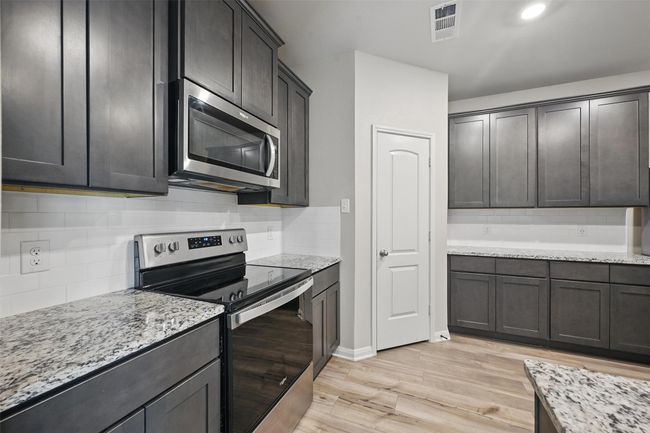 Kitchen featuring backsplash, light wood-type flooring, appliances with stainless steel finishes, and light stone counters | Image 8