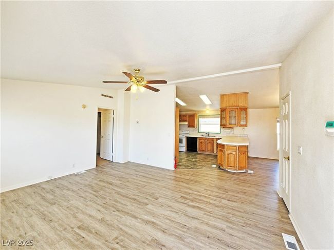 Unfurnished living room featuring light wood-style floors, ceiling fan, visible vents, and a sink | Image 5