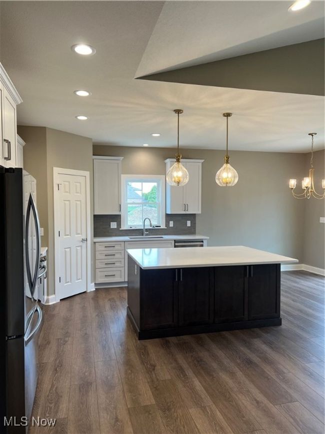 Kitchen with fridge, light countertops, a kitchen island, dark wood-type flooring, and white cabinetry | Image 7