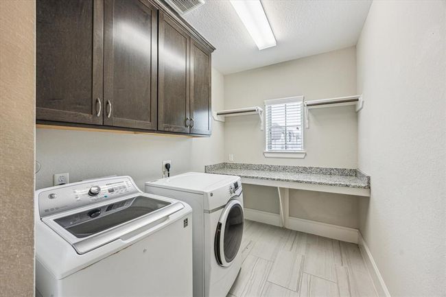 This laundry room is spacious and bright with ample cabinetry and a countertop with storage space. A small window provides natural light, enhancing the room’s functionality. | Image 28