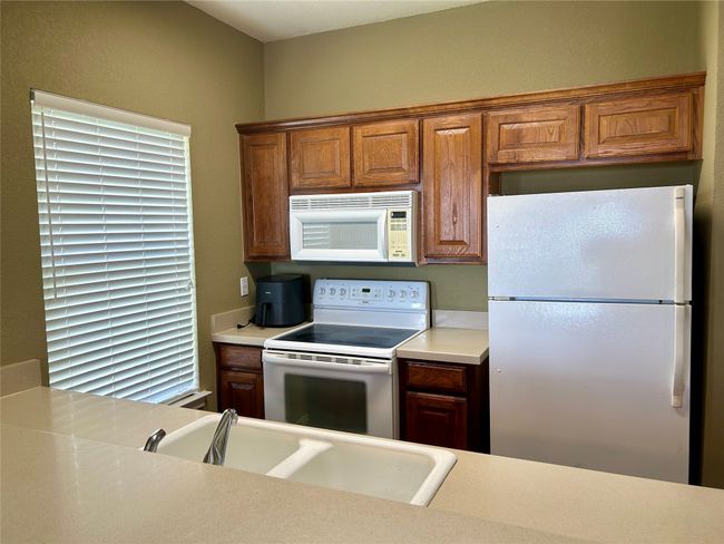 Kitchen featuring white appliances, light countertops, a sink, and brown cabinets | Image 12