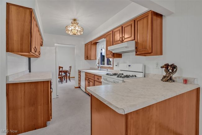 Kitchen featuring under cabinet range hood, white appliances, a sink, brown cabinets, and a chandelier | Image 13