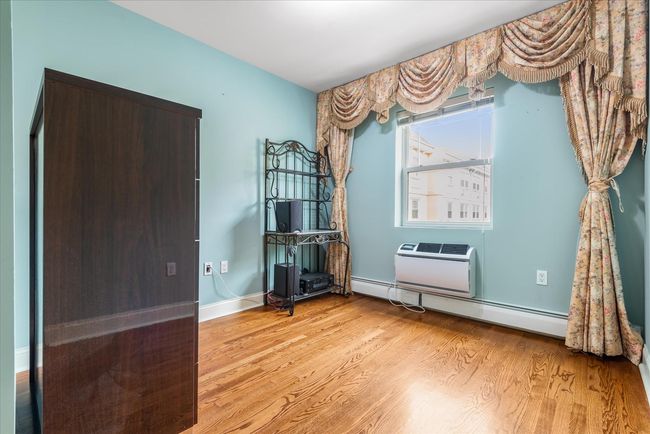 Misc room with a wall mounted AC, a baseboard radiator, wood finished floors, and baseboards | Image 13