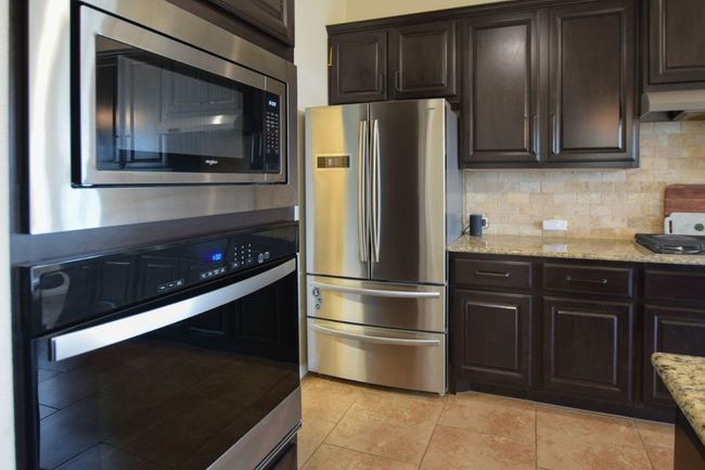 Kitchen featuring dark brown cabinetry, light stone countertops, backsplash, and appliances with stainless steel finishes | Image 5