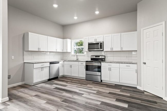 Kitchen featuring white cabinets, appliances with stainless steel finishes, light stone counters, and a high ceiling | Image 10