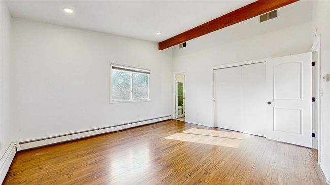 Unfurnished bedroom with wood finished floors, visible vents, a baseboard radiator, vaulted ceiling with beams, and a closet | Image 14
