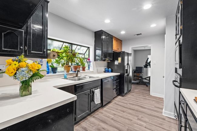 Kitchen featuring stainless steel dishwasher, a sink, black fridge, light wood-style floors, and dark cabinetry | Image 10