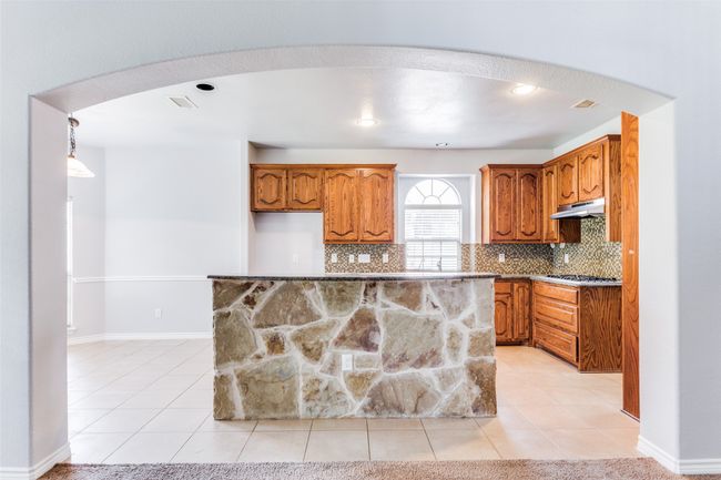 Kitchen featuring under cabinet range hood, brown cabinets, arched walkways, and light tile patterned floors | Image 11