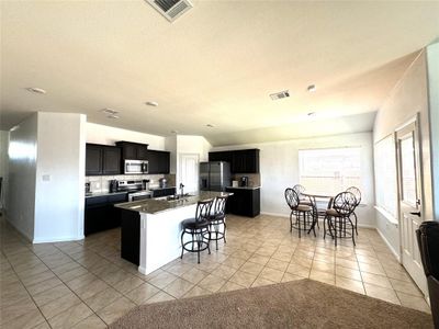 Kitchen featuring light tile patterned floors, stainless steel appliances, sink, an island with sink, and a breakfast bar | Image 2