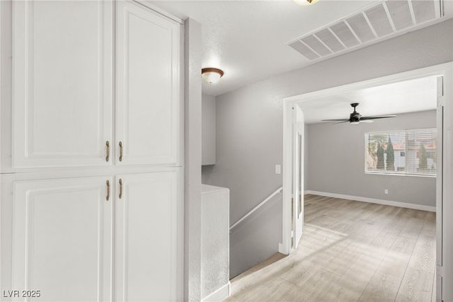 Hallway with light wood-type flooring, visible vents, baseboards, and an upstairs landing | Image 22