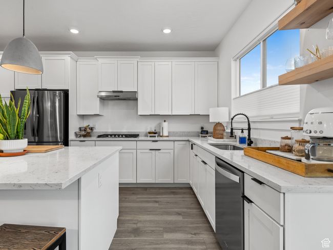 Kitchen featuring appliances with stainless steel finishes, under cabinet range hood, white cabinetry, recessed lighting, and decorative light fixtures | Image 40