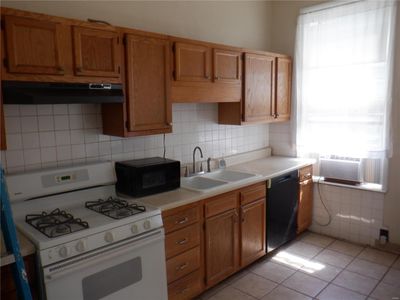 Kitchen with light tile patterned flooring, sink, range hood, cooling unit, and black appliances | Image 3