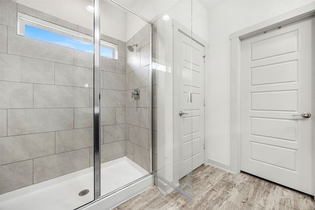 A full view of the walk-in shower in the primary bathroom, featuring stylish tile work, a sliding glass door, and a privacy window. | Image 18