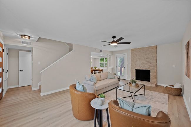 Living area featuring a stone fireplace, light wood finished floors, new baseboards, stairs, and a ceiling fan | Image 4