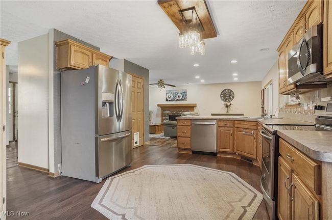 Kitchen with dark wood-style floors, a peninsula, stainless steel appliances, and a fireplace | Image 12