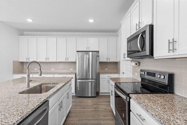 Kitchen with white cabinetry, stainless steel appliances, dark wood-type flooring, decorative backsplash, and a sink | Image 10