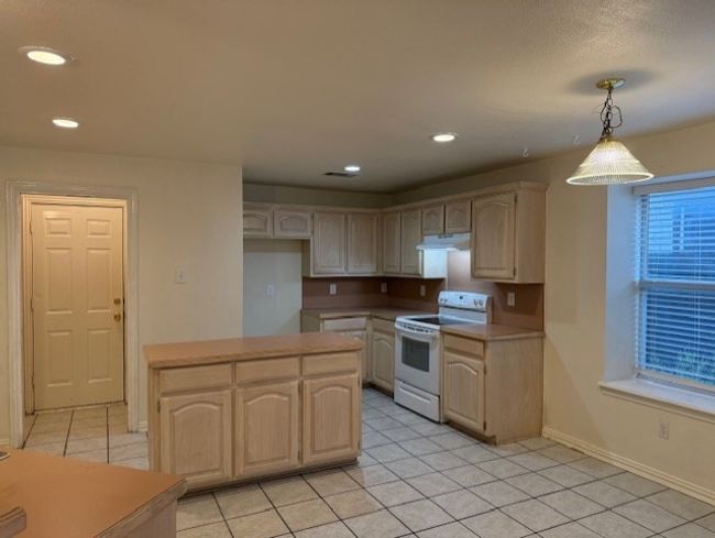 Kitchen with white electric range, light tile patterned floors, recessed lighting, light countertops, and light brown cabinetry | Image 7