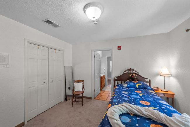 Bedroom with a textured ceiling, connected bathroom, visible vents, light carpet, and a closet | Image 23