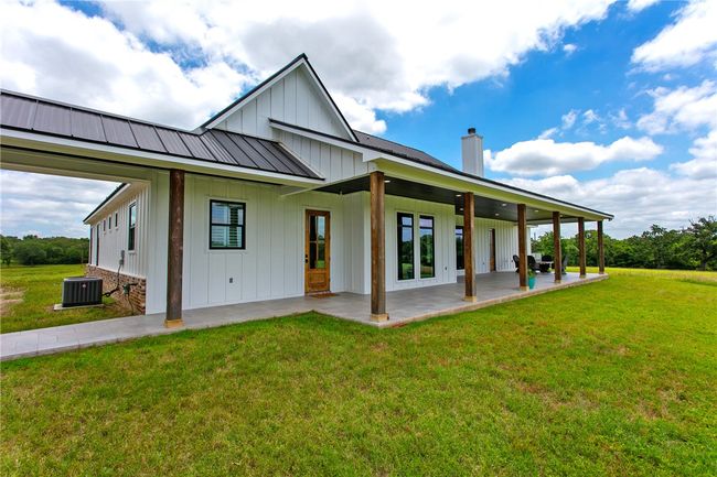 Back of house featuring board and batten siding, a chimney, a lawn, a patio area, and metal roof | Image 29