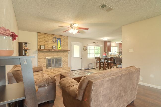 Living room with a ceiling fan, a textured ceiling, dark wood-style floors, and a brick fireplace | Image 10