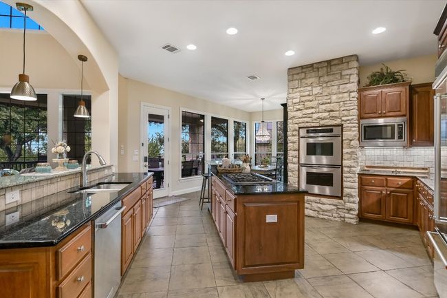 Spacious Kitchen featuring stainless steel Thermador ovens and cooktop with Kitchenaid refrigerator and dishwasher, a center island, dark stone countertops, pecan cabinets, and Travertine backsplash | Image 9