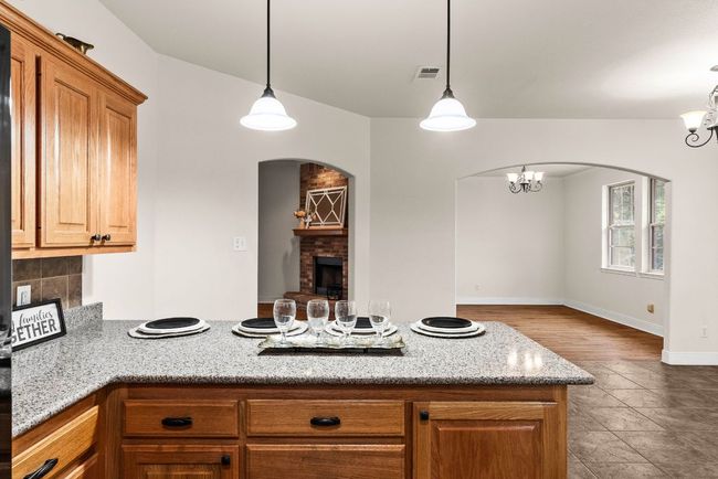 Kitchen featuring visible vents, arched walkways, a brick fireplace, a peninsula, and light stone countertops | Image 16