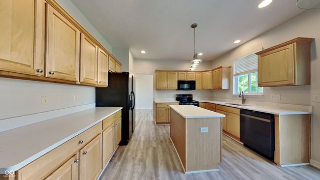 kitchen featuring black appliances, a sink, light brown cabinets, light wood-style flooring, and a kitchen island | Image 7