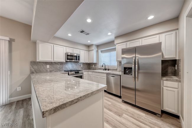 Kitchen with appliances with stainless steel finishes, a peninsula, white cabinetry, light wood finished floors, and backsplash | Image 15
