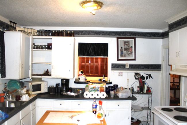 Kitchen featuring white microwave, white cabinets, dark countertops, a sink, and a textured ceiling | Image 11