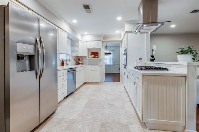 This kitchen features modern stainless steel appliances, ample white cabinetry, and a spacious layout with travertine tiled flooring. It has a Kitchen Aid gas cooktop, Kitchen Aid Single Oven, Vent and a bright, inviting atmosphere, perfect for cooking and entertaining. | Image 12