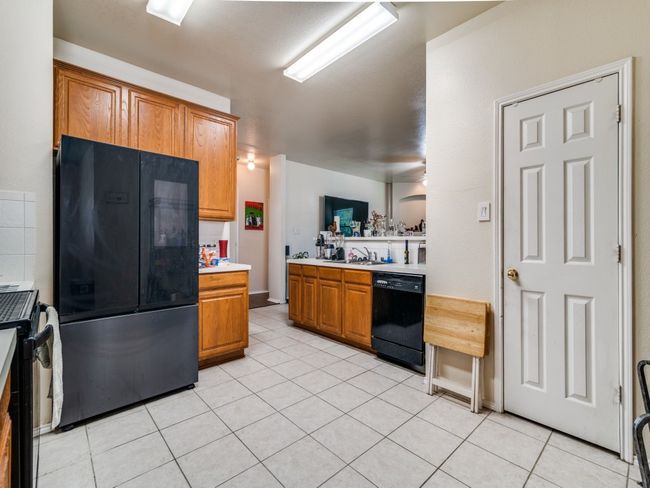 Kitchen featuring a sink, brown cabinetry, black appliances, light tile patterned flooring, and light countertops | Image 9