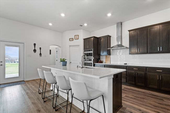 Kitchen with a sink, stainless steel double oven, a kitchen island with sink, arched walkways, and wall chimney exhaust hood | Image 14