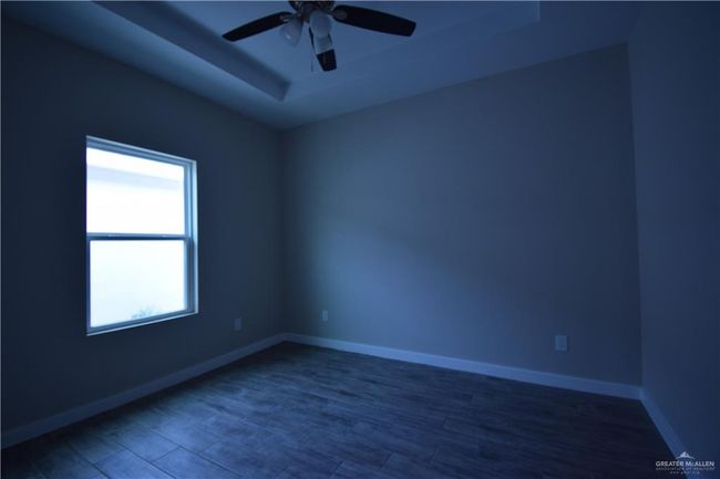 Unfurnished room featuring a tray ceiling, ceiling fan, wood finished floors, and baseboards | Image 4