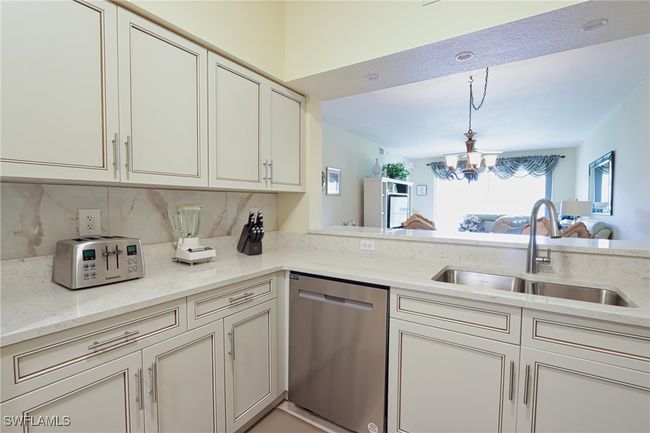 Kitchen featuring light stone countertops, dishwasher, an inviting chandelier, backsplash, and sink | Image 8