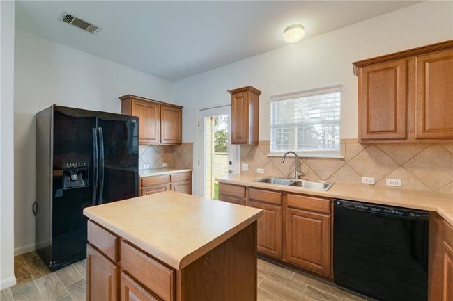 Kitchen with black appliances, a sink, a center island, light countertops, and backsplash | Image 9