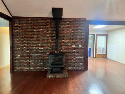 Unfurnished living room with wood-type flooring, a textured ceiling, a wood stove, brick wall, and lofted ceiling | Image 2