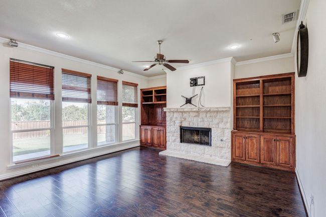Unfurnished living room featuring ceiling fan, dark hardwood / wood-style flooring, a stone fireplace, and ornamental molding | Image 17