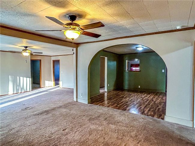 Unfurnished room with ornamental molding, arched walkways, dark carpet, and a ceiling fan | Image 8