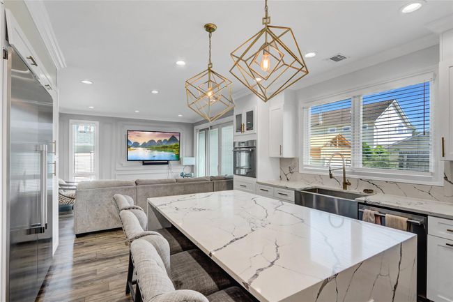 Kitchen with a chandelier, black oven, ornamental molding, a sink, and a center island | Image 9